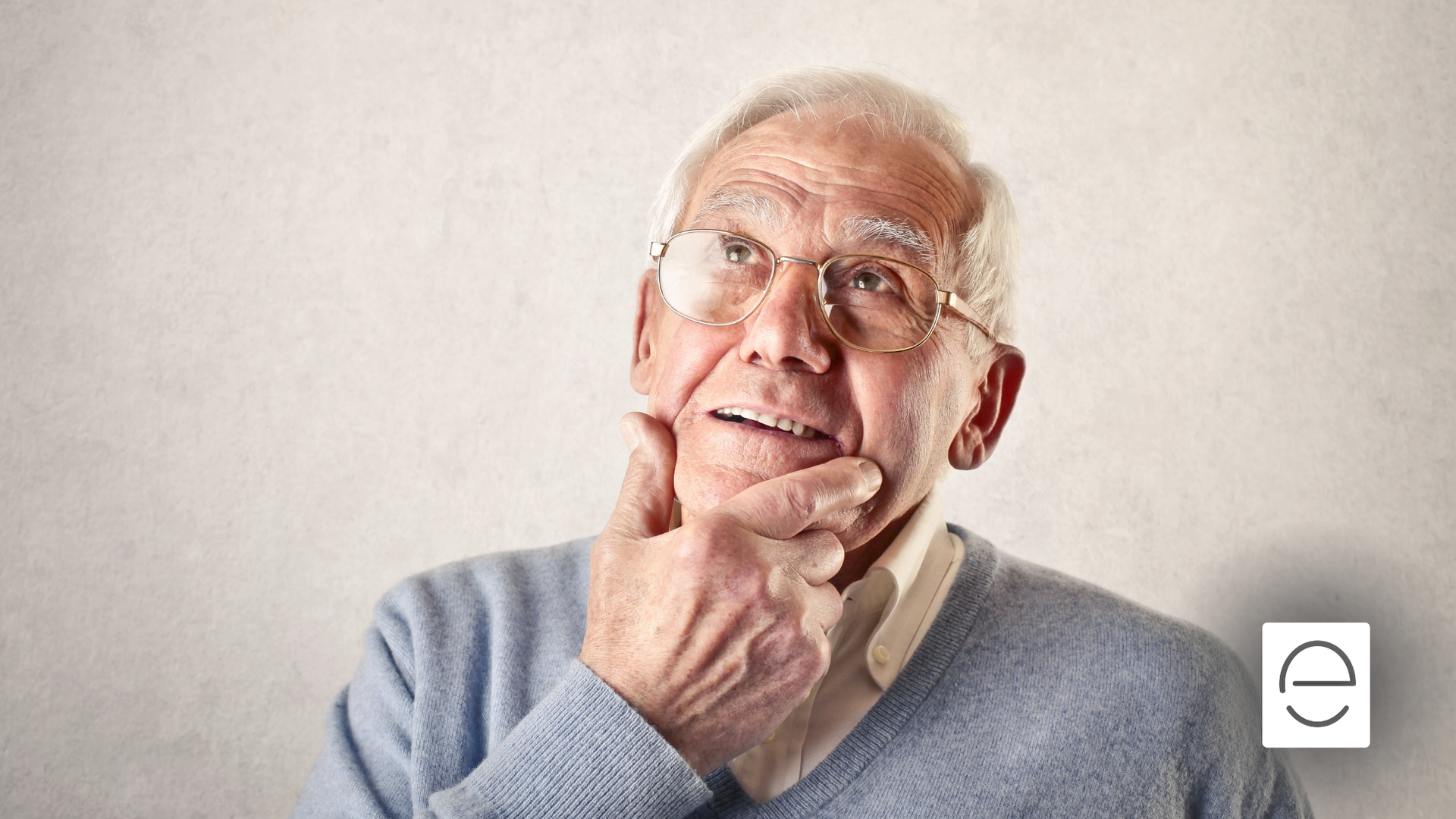 Man in glasses, light blue sweater, touching chin, looking upward thoughtfully against a white background.