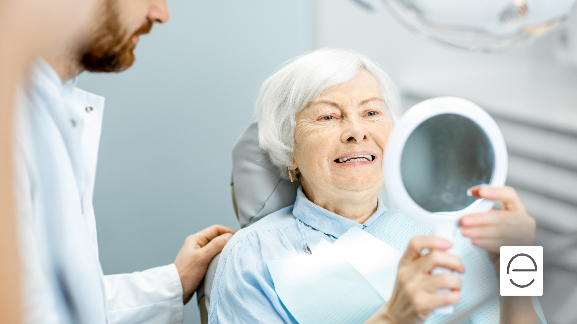 Dentist shows older patient her teeth with a mirror. She smiles in a dental office.