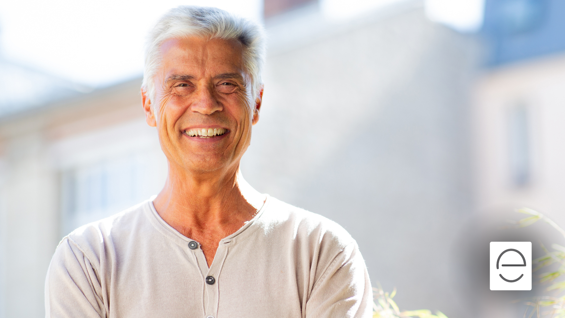 Smiling man outdoors in a light-colored shirt, with buildings in the blurred background.
