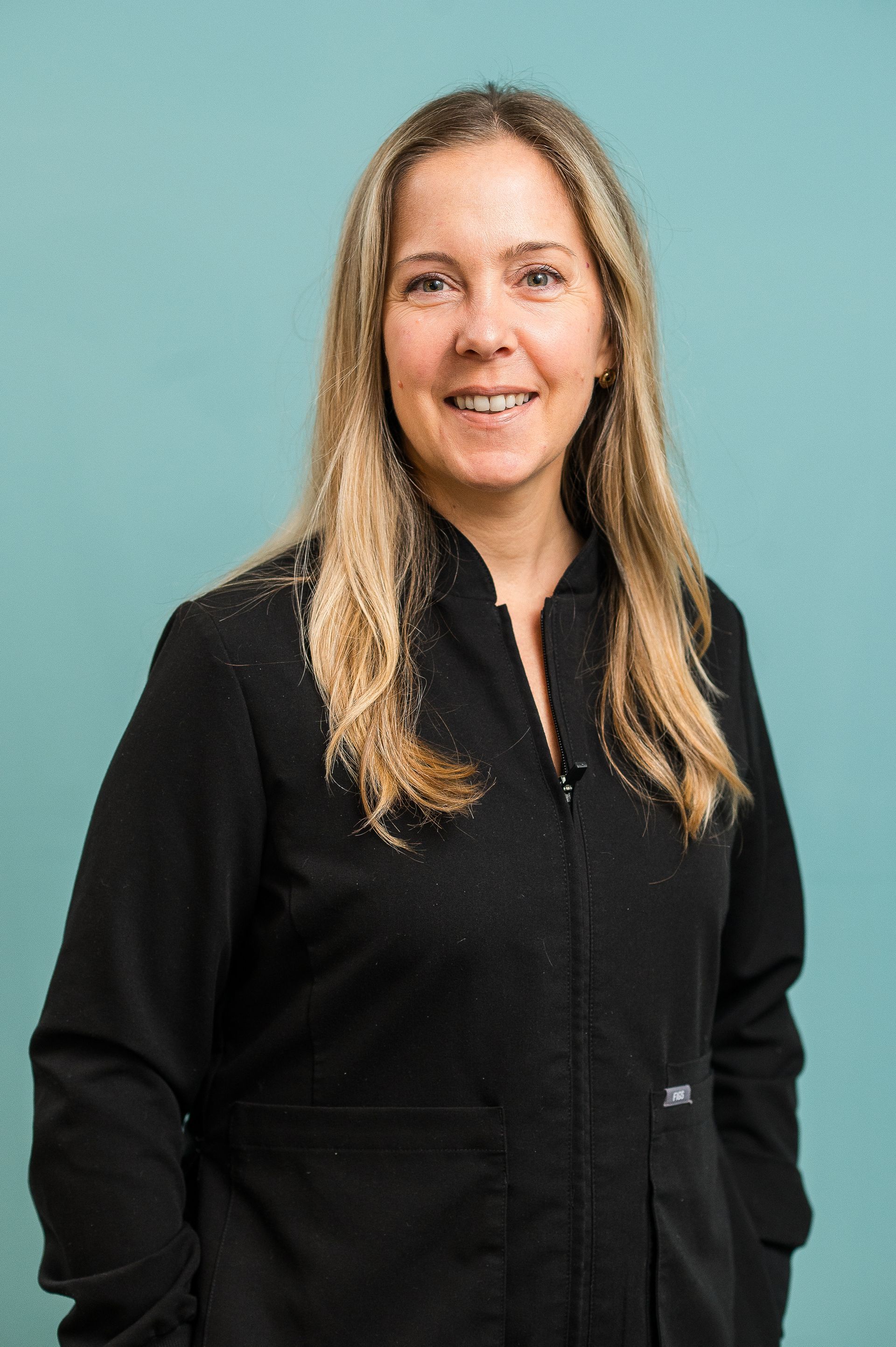 Woman in a black zip-up top smiling against a teal background