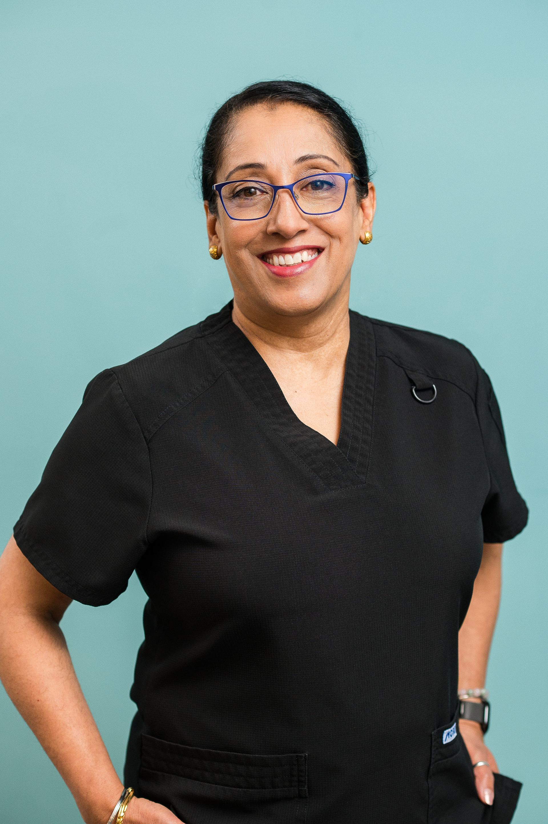 Smiling person in black shirt and glasses standing against a light blue background.