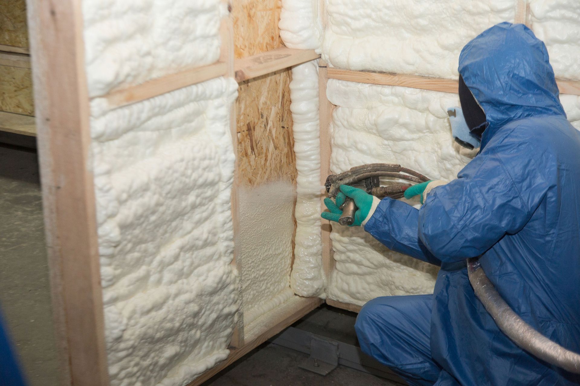 Worker in blue suit spraying foam insulation on wooden wall frame. Worker in blue suit spraying foam insulation on wooden wall frame.