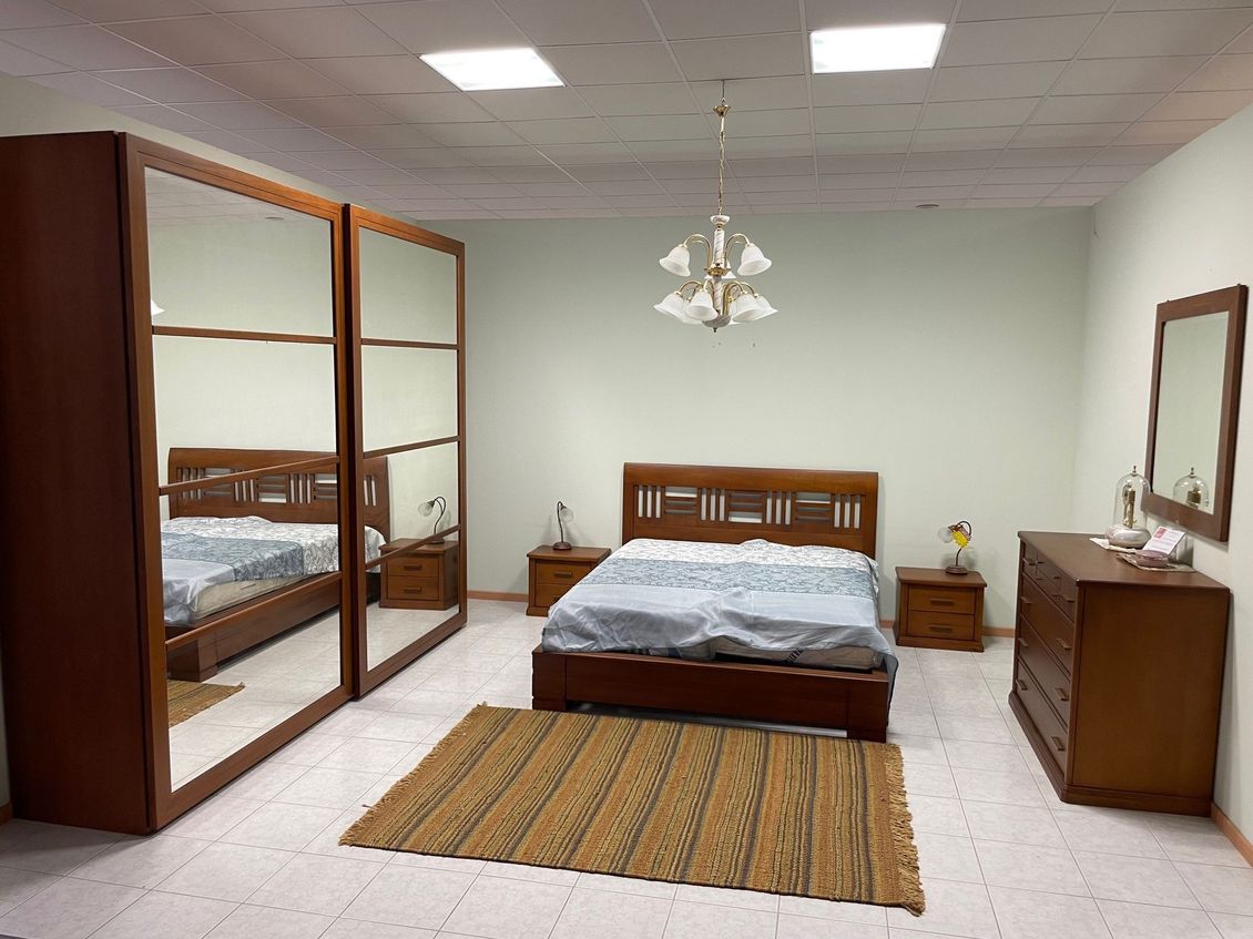 Una camera da letto con letto, cassettiera, comodino, specchio e armadio.