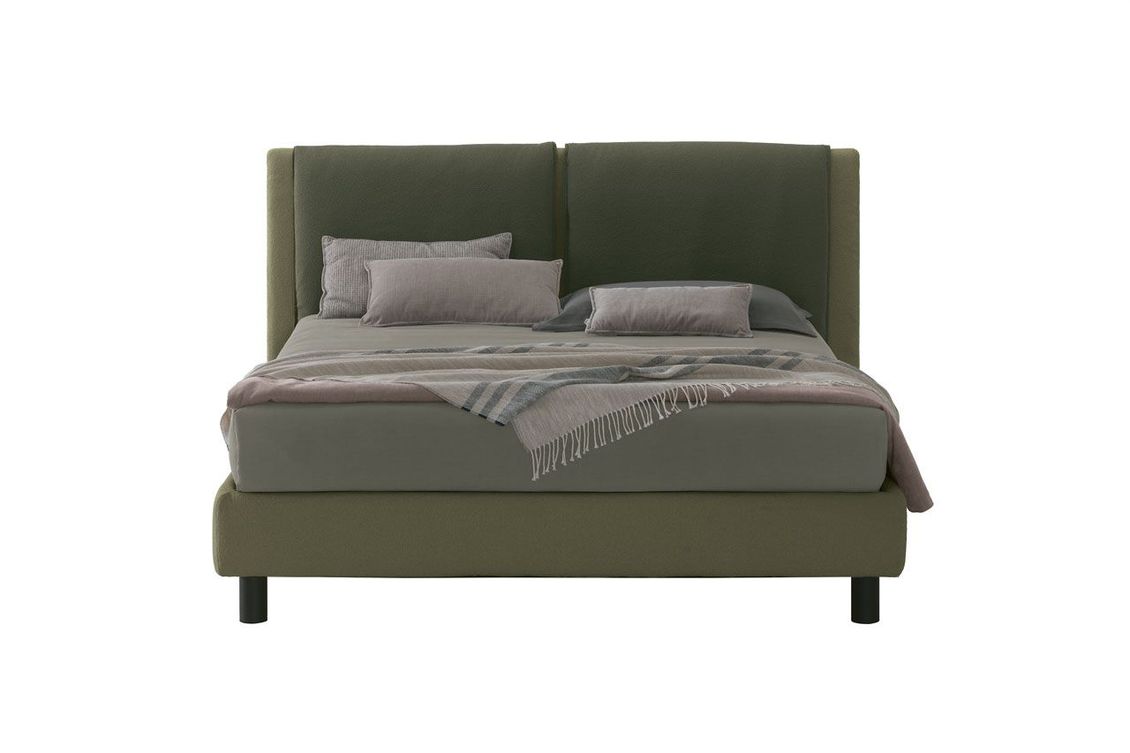 Un letto con testiera verde e cuscini su sfondo bianco.