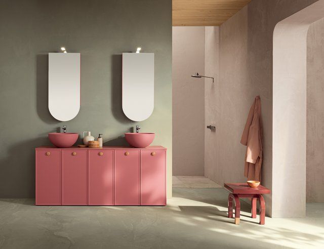 Un bagno con mobili rosa, due lavandini, due specchi e uno sgabello.
