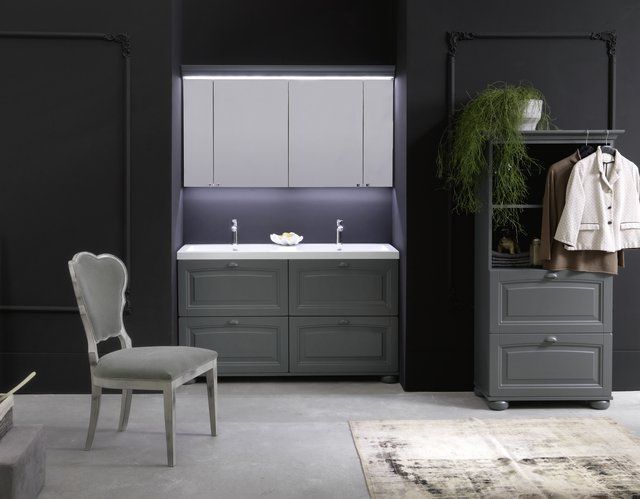 Un bagno con lavandino, cassettiera, sedia e appendiabiti.