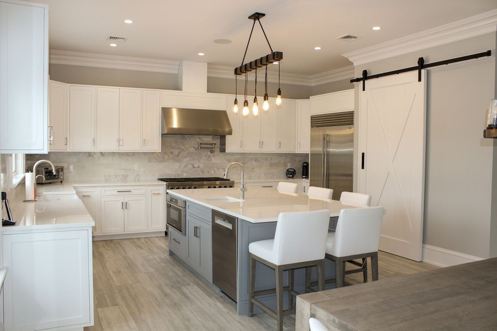 A modern kitchen featuring white cabinets, a gray center island with bar stools, stainless appliances, and a barn door.