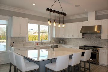 A bright kitchen with white cabinets, a large central island with white seating, and a modern wooden pendant light fixture.