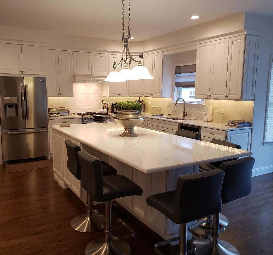 White kitchen with island, marble countertop, bar stools, stainless steel appliances, and pendant light.