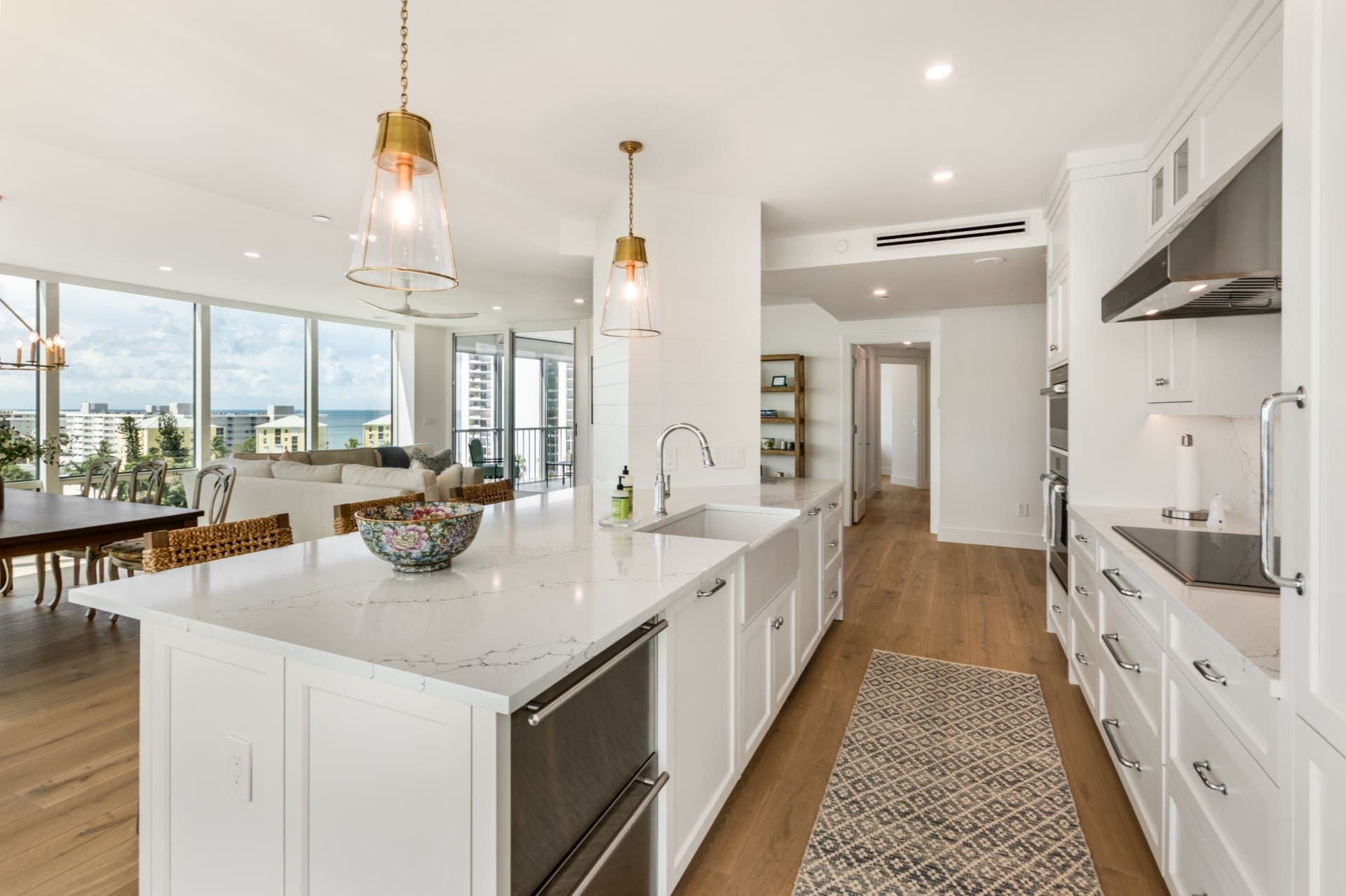 Bright modern kitchen with white island, pendant lights, and large windows overlooking a city view