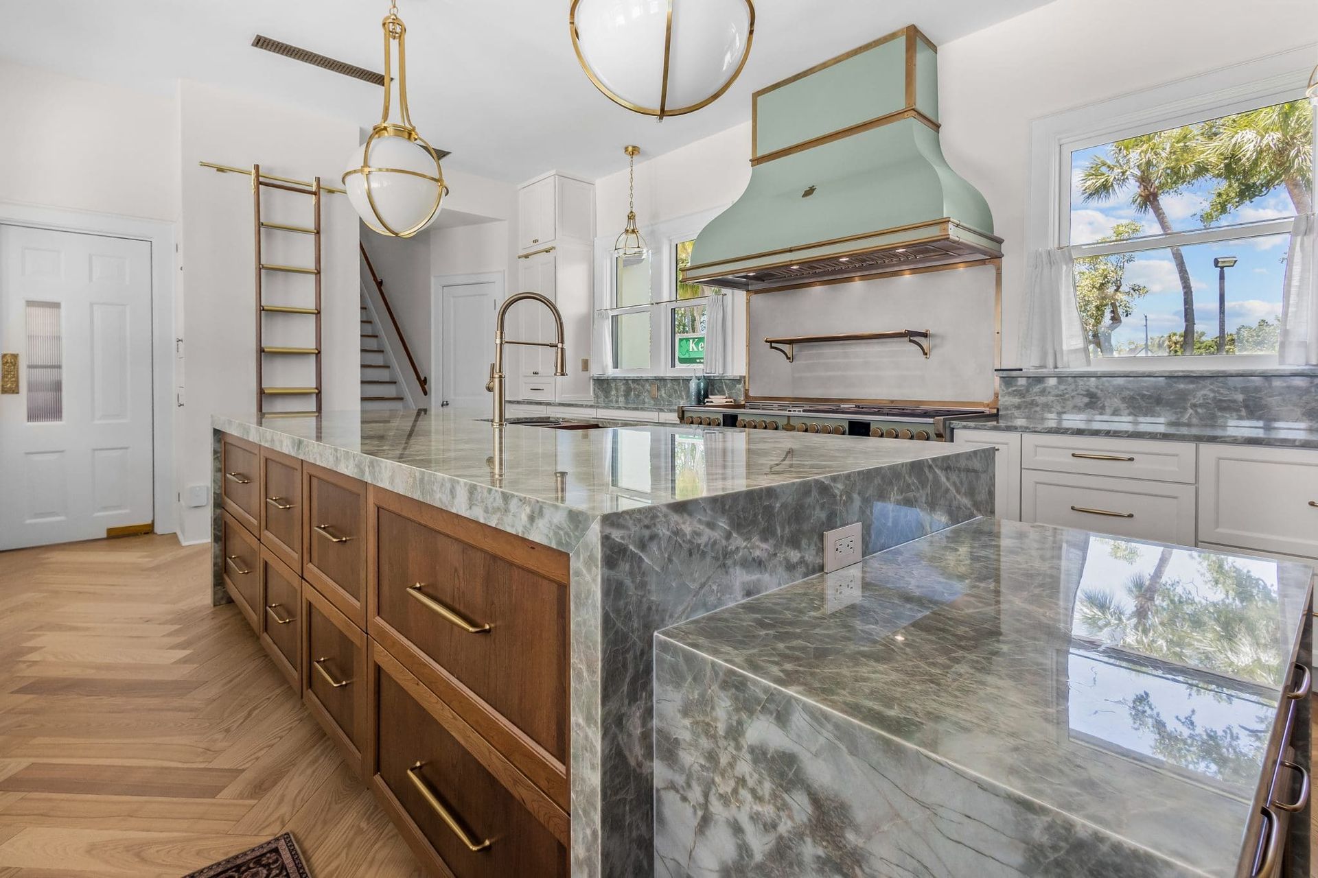 Bright modern kitchen with marble island, wood cabinets, gold fixtures, and turquoise range hood