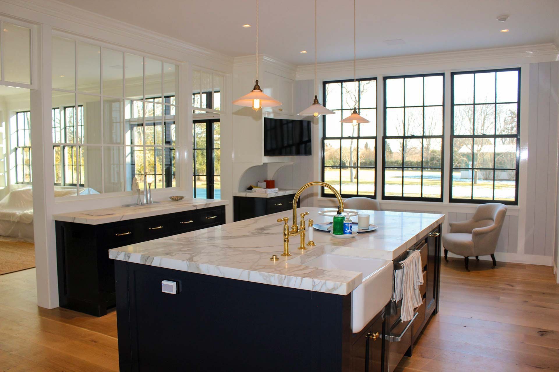 Modern kitchen with blue island, white countertop, gold faucet, and large windows.