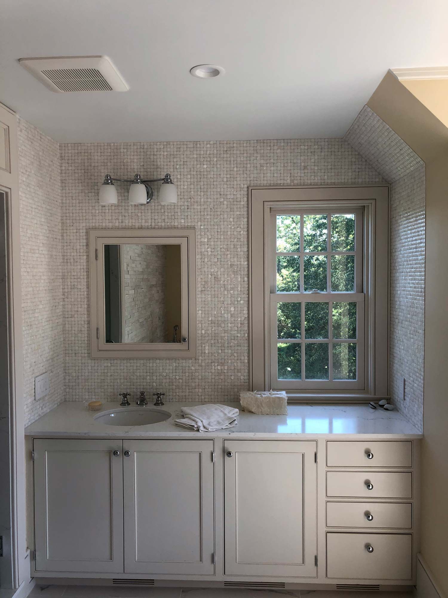 Bathroom with vanity, mirror, window, and textured wall tiles. Light wood cabinets and trim.