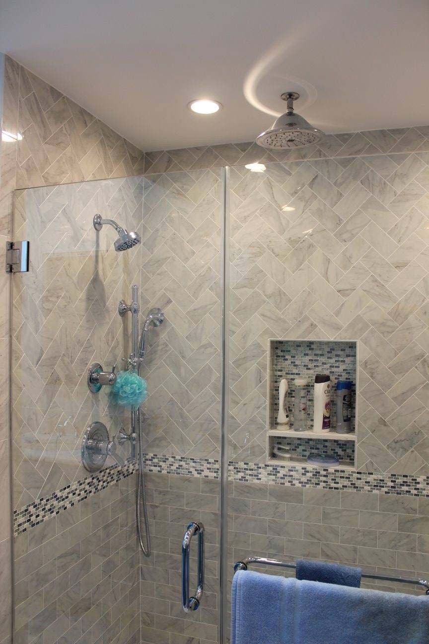 A modern shower with glass doors and grey tile, featuring a built-in shelf and showerheads.
