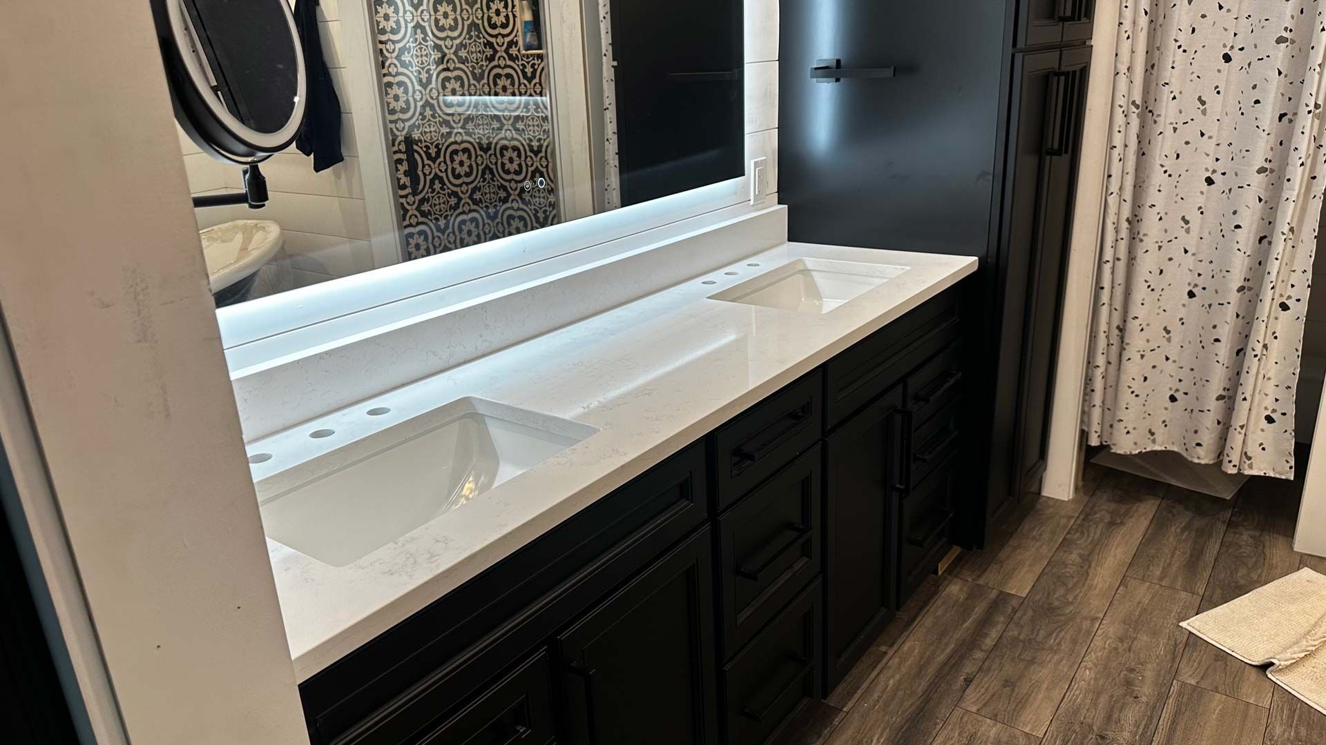 Black double vanity with white countertop and sinks.  Bathroom with a mirror, shower curtain, and wood-look floor.