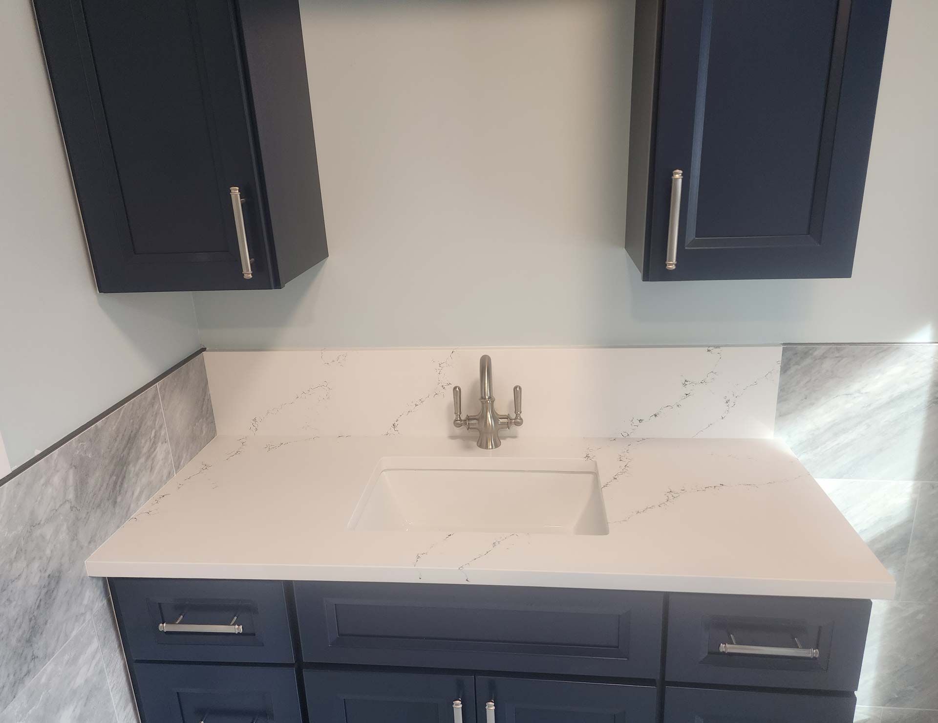 Navy blue vanity with a white countertop and cabinets. A stainless steel faucet sits above the sink.