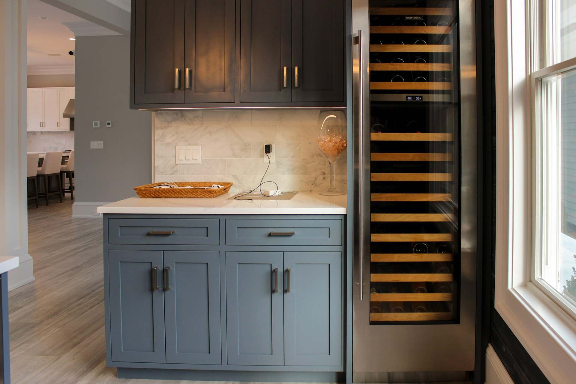 Gray and blue cabinets in a kitchen area with a wine cooler and a marble countertop.