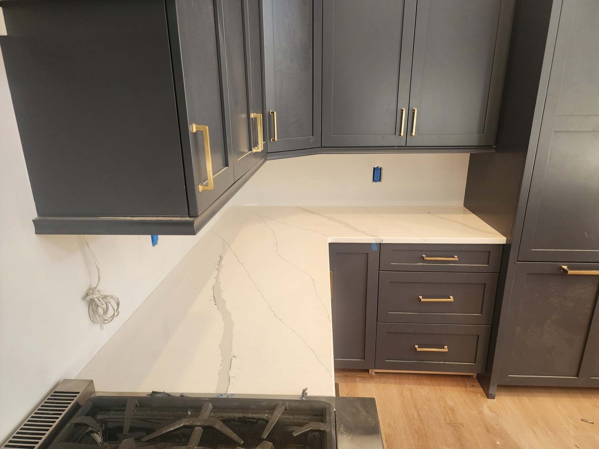 Dark gray kitchen cabinets with gold handles, white countertop, and a gas stove.