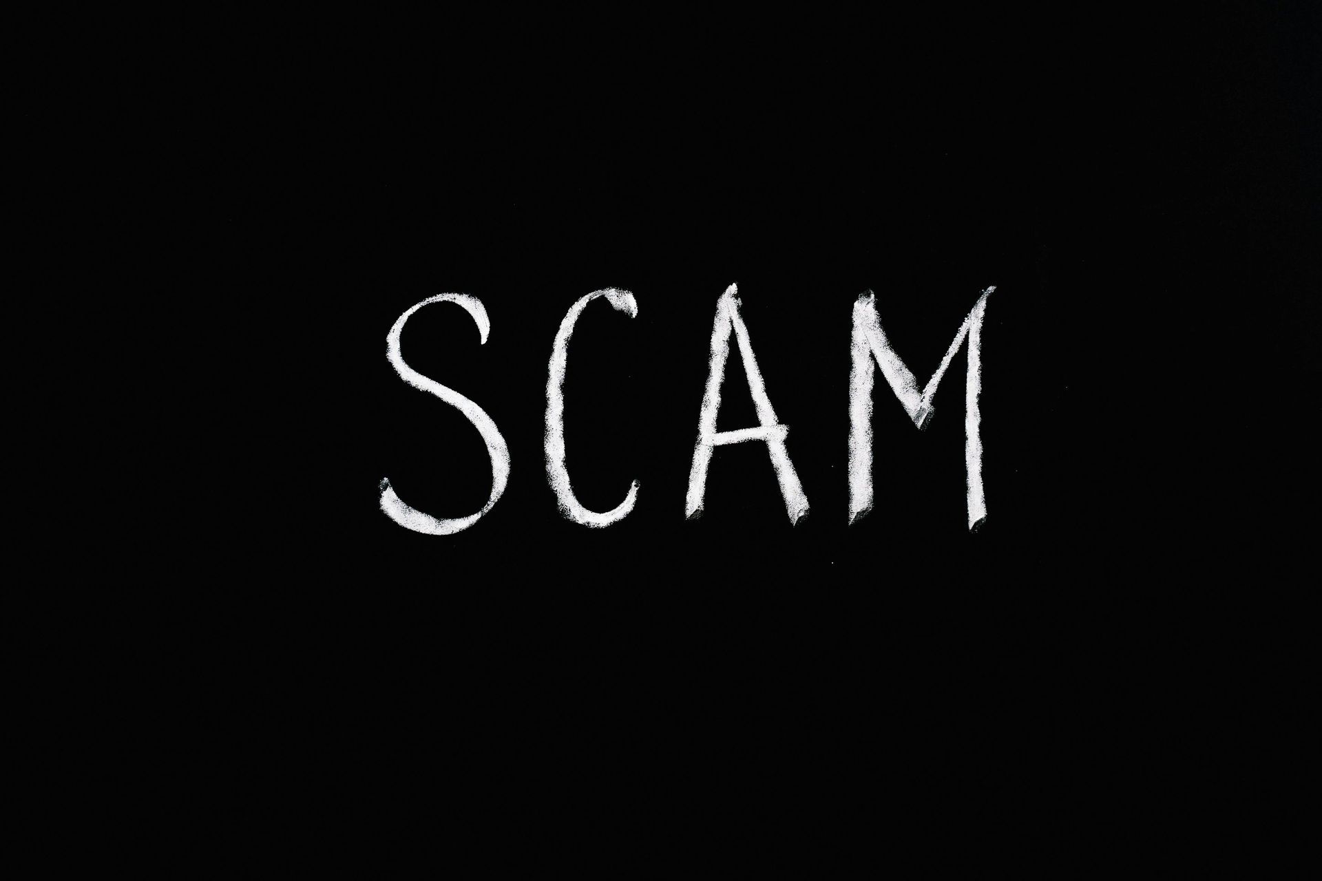 White chalk writing SCAM on a black background.