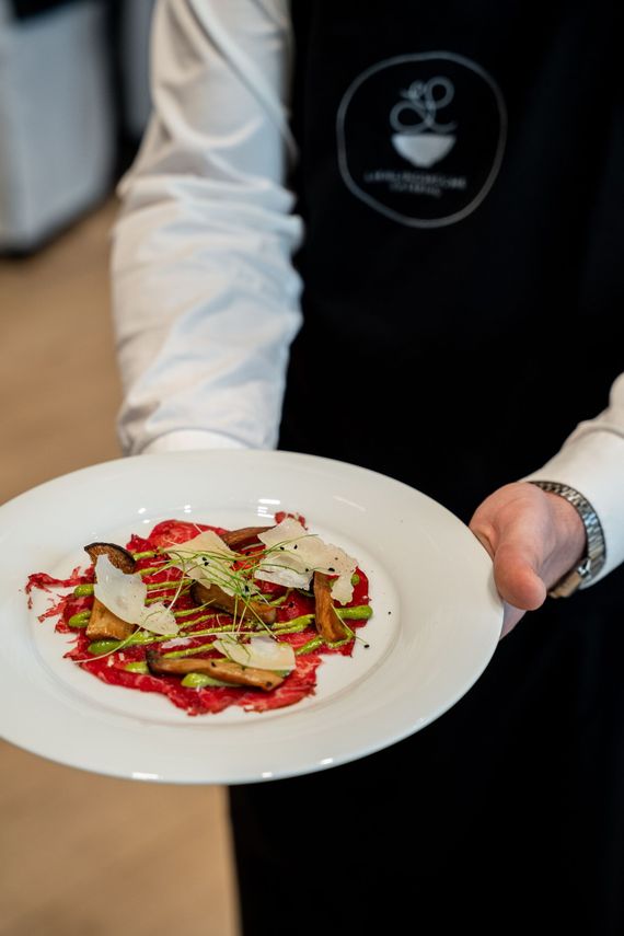 Ein Kellner hält einen weißen Teller mit einem angerichteten Gourmetgericht und roter Soße.