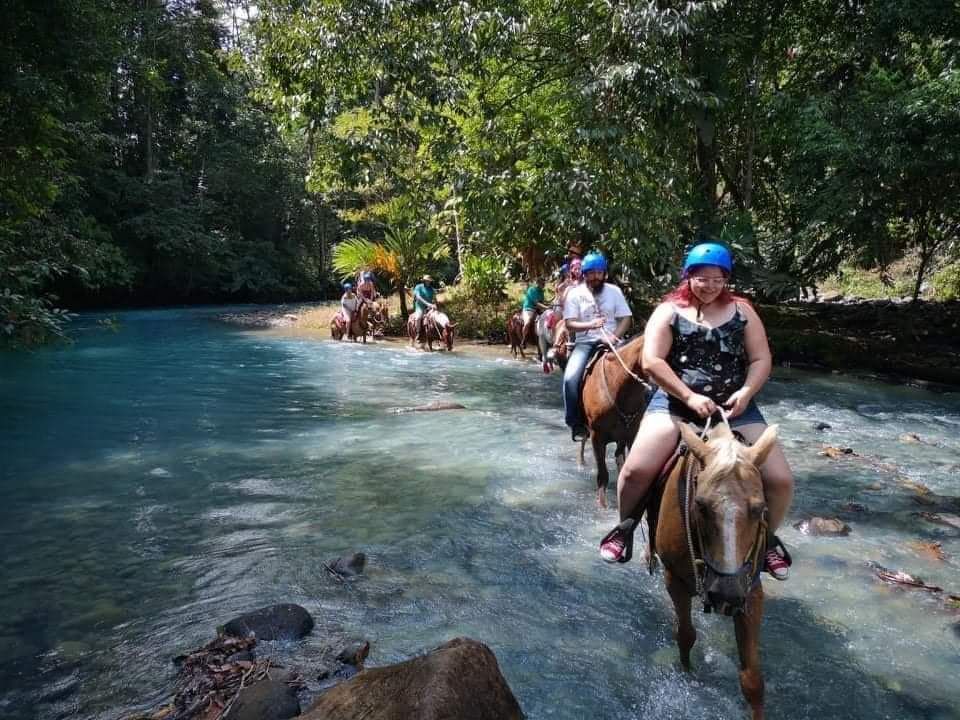 Guided horseback riding group crossing a scenic river while exploring tropical landscapes and nature in Costa Rica