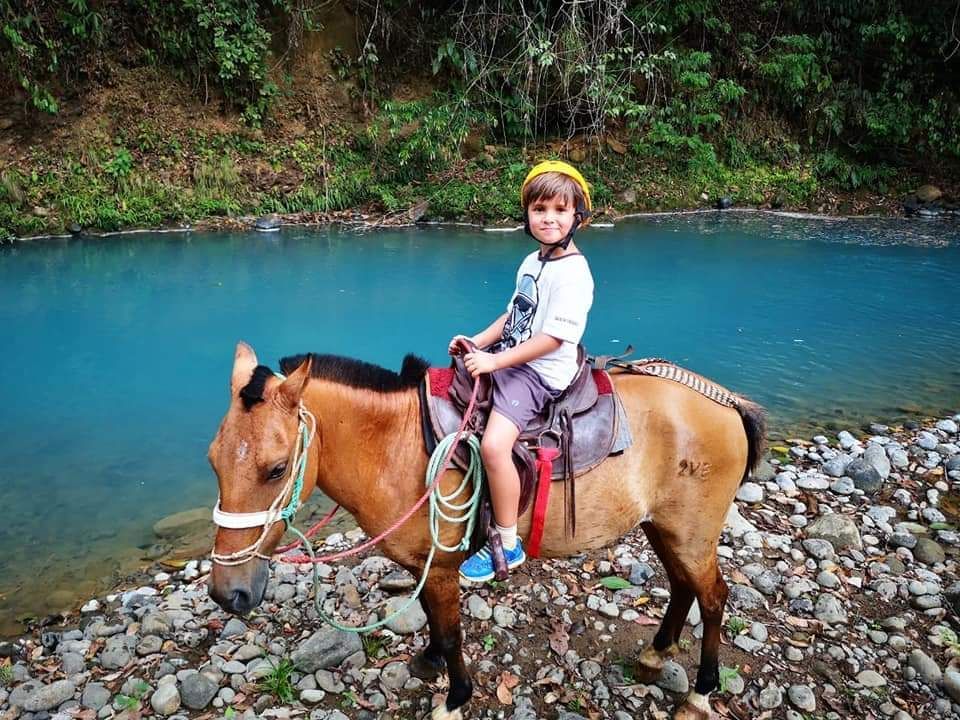 Young rider enjoying a horseback riding experience beside a tropical river surrounded by beautiful Costa Rica nature