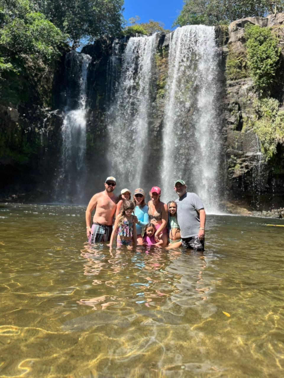 Family swimming beneath Llanos de Cortés Waterfall in Costa Rica.