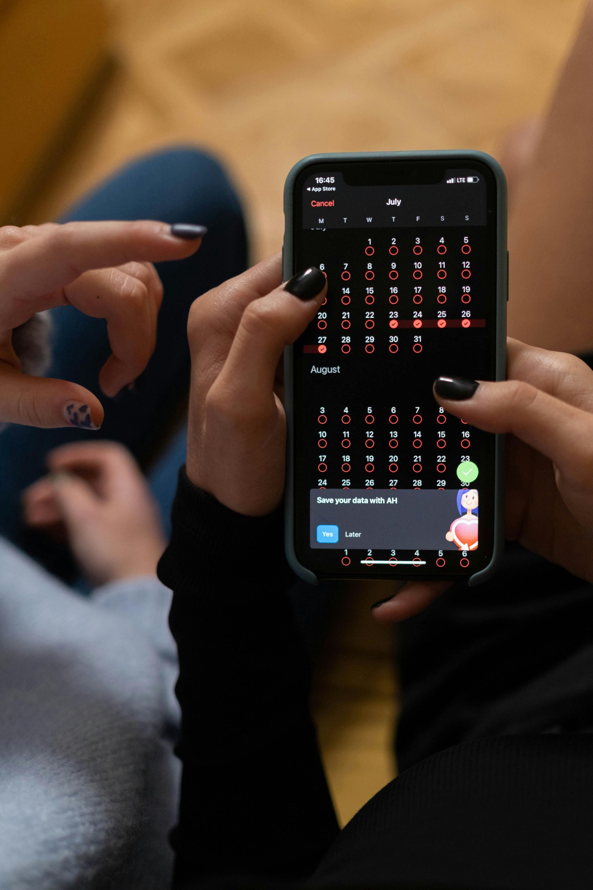 Person using a smartphone with black nail polish; another person's finger is pointing at the screen.
