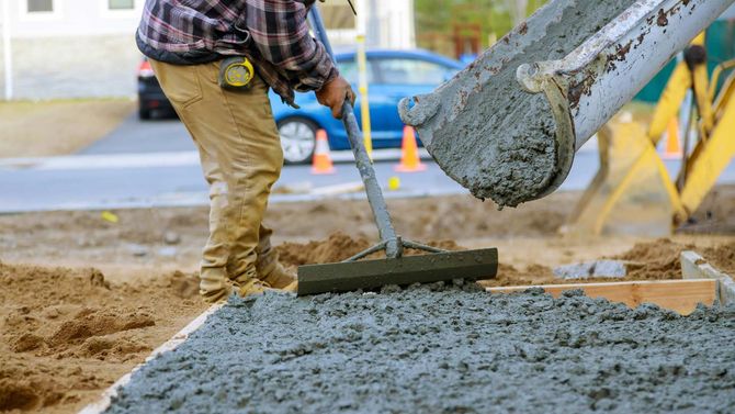 A man is raking concrete on a construction site.