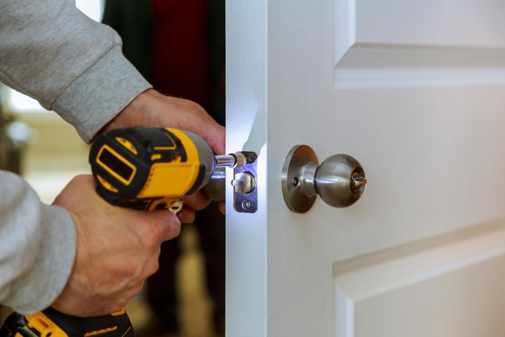 A Man Is Fixing a Door with A Drill — Tropical Locksmiths in Proserpine, QLD