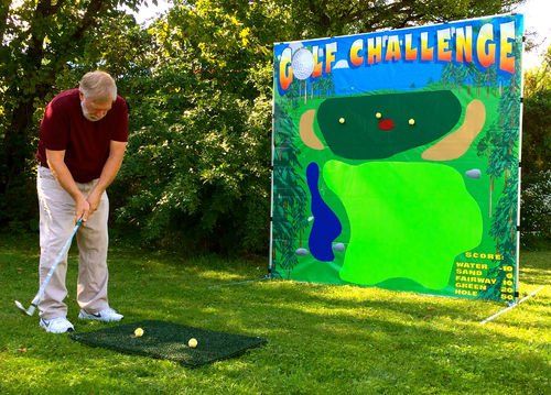 A man playing a golf challenge game at an outdoor event, standing on a mat and aiming at a colorful target backdrop.