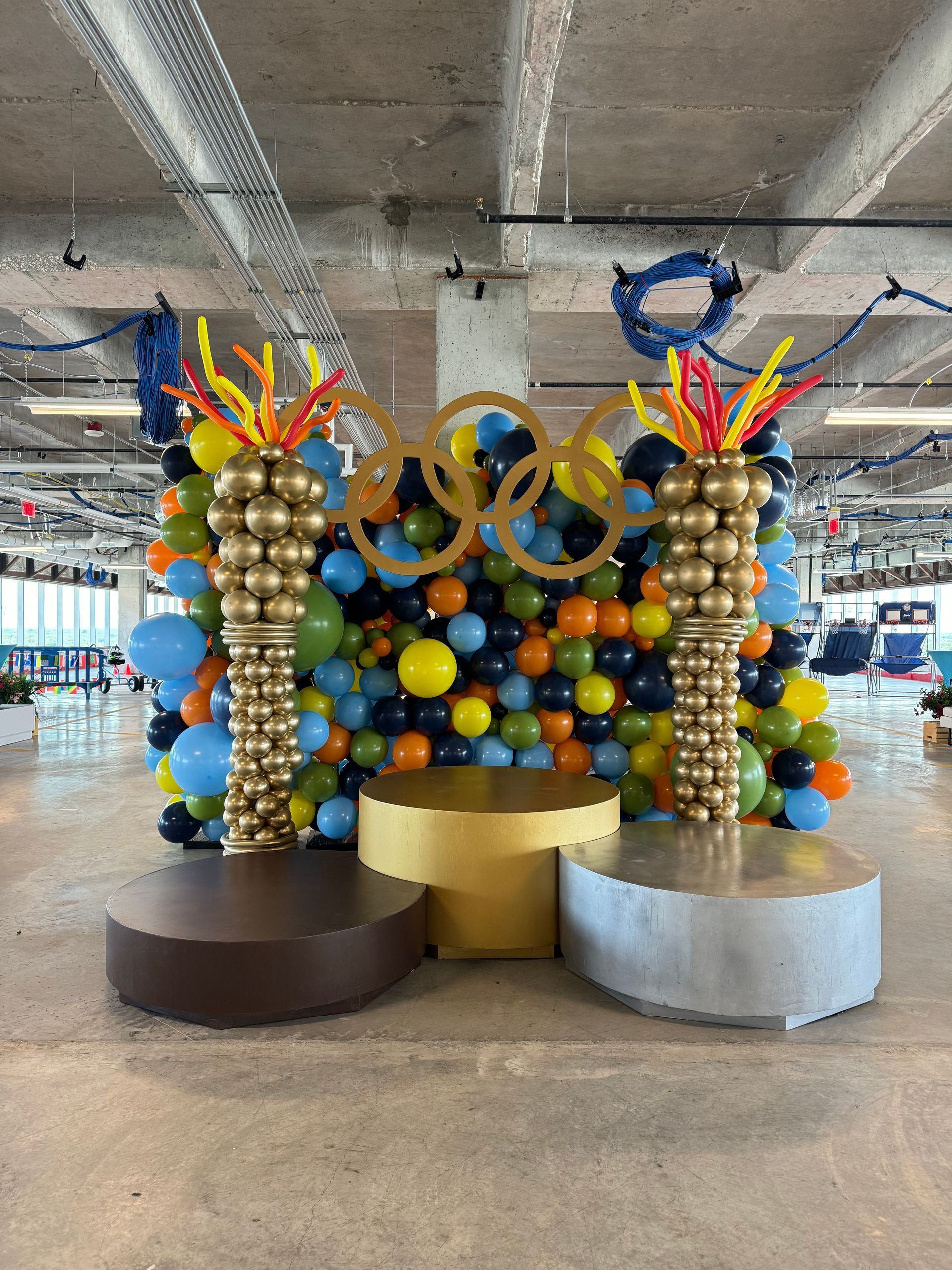 Olympic-themed balloon display with gold, blue, and multicolor balloons and a podium.