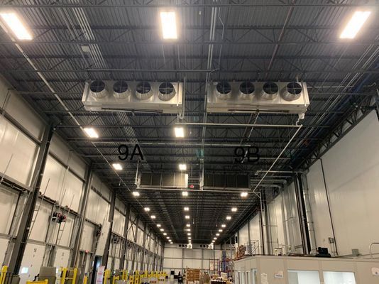 Two large commercial industrial air cooling units suspended from the ceiling in a high-bay warehouse.