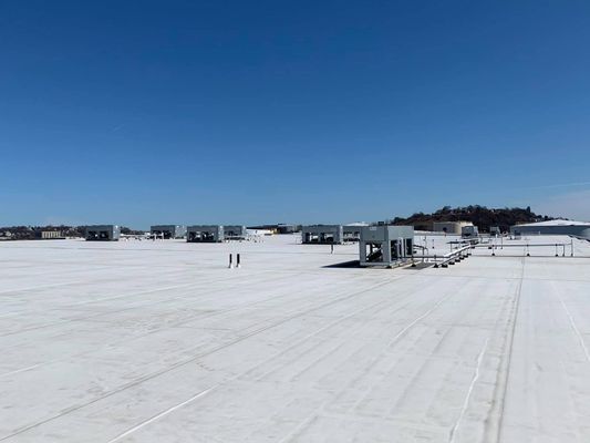 A wide, flat white industrial roof under a clear blue sky with several HVAC units scattered across the surface.