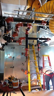 A detailed view of red-painted industrial piping and valves connected to a large silver HVAC unit indoors.