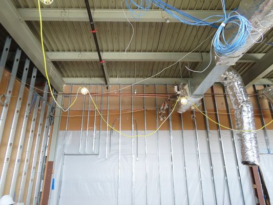 Construction site interior with metal wall studs, exposed ceiling beams, electrical wiring, and suspended ductwork.