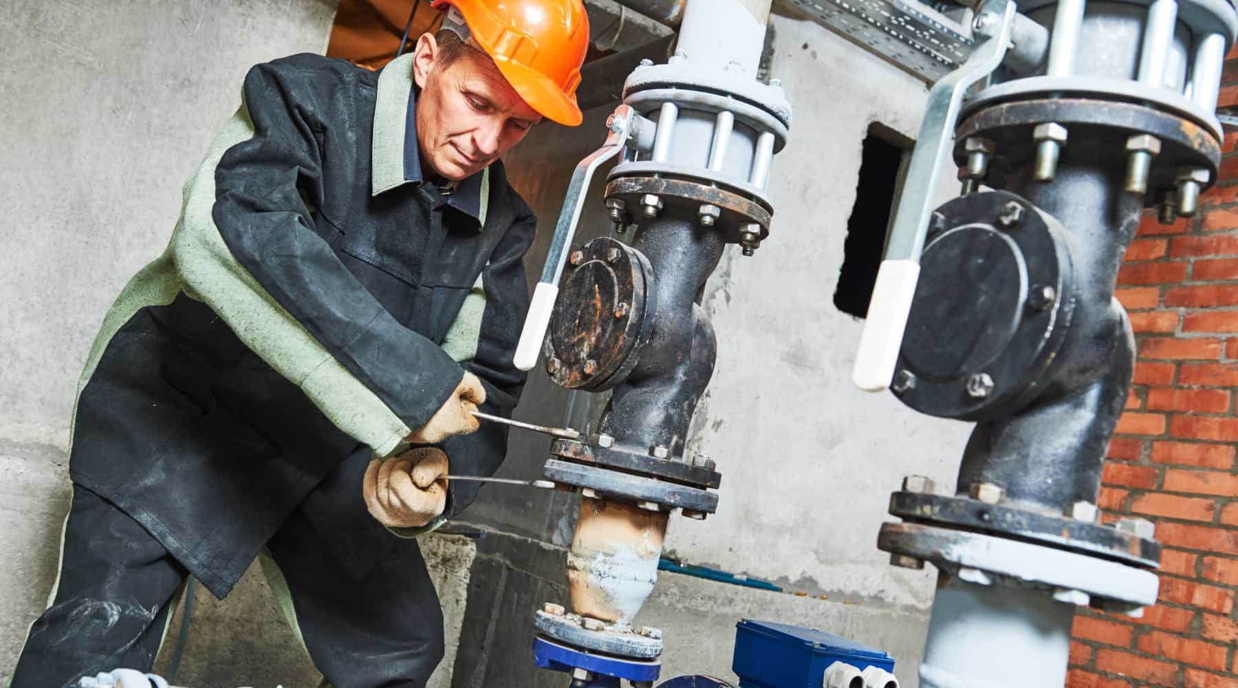 Worker in orange hard hat adjusting industrial pipes with a wrench in a factory setting