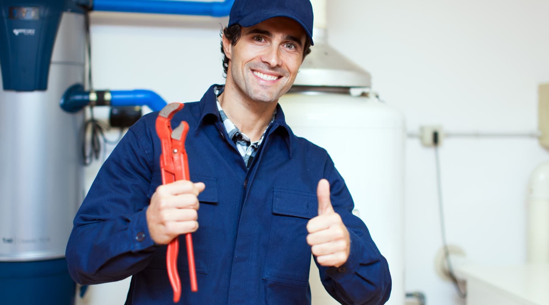 Smiling technician in blue coveralls holding red pliers and giving a thumbs-up in a workshop