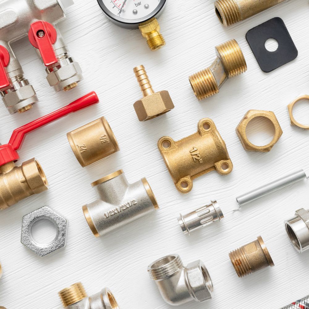 Assorted brass plumbing fittings, valves, and gauge parts on a white surface