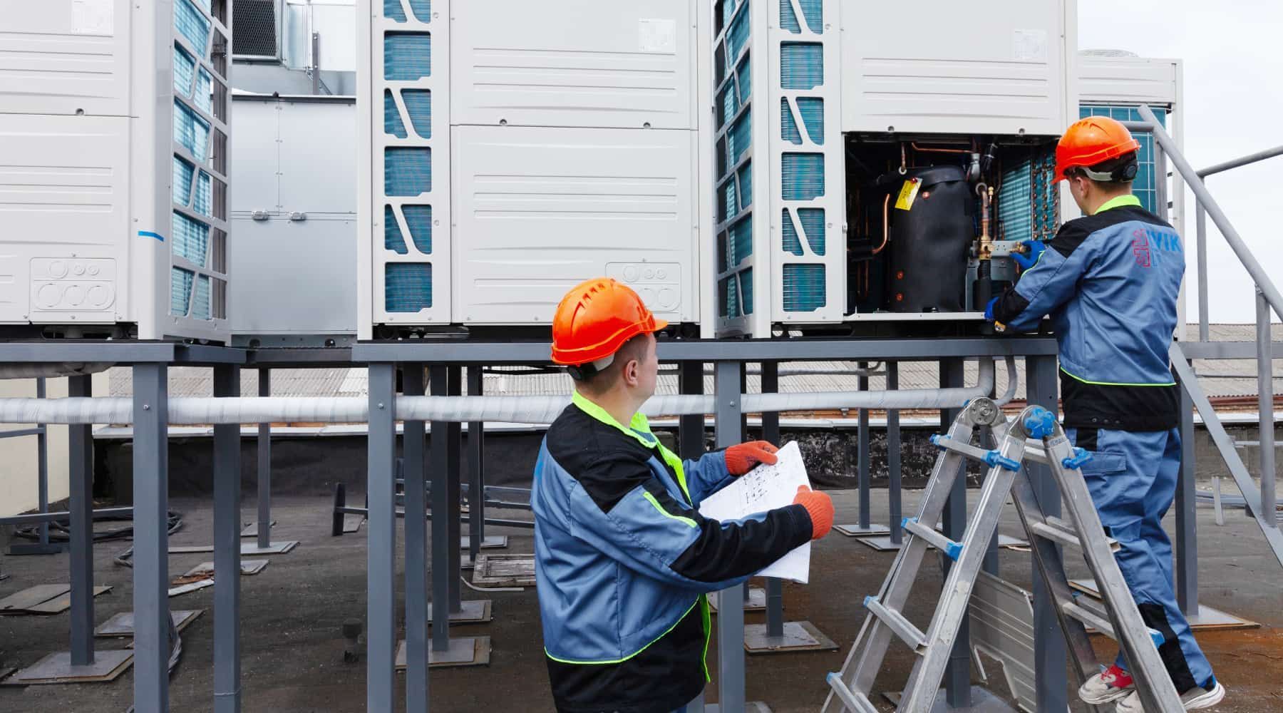 Workers in orange hard hats installing equipment on a metal platform beside industrial tanks