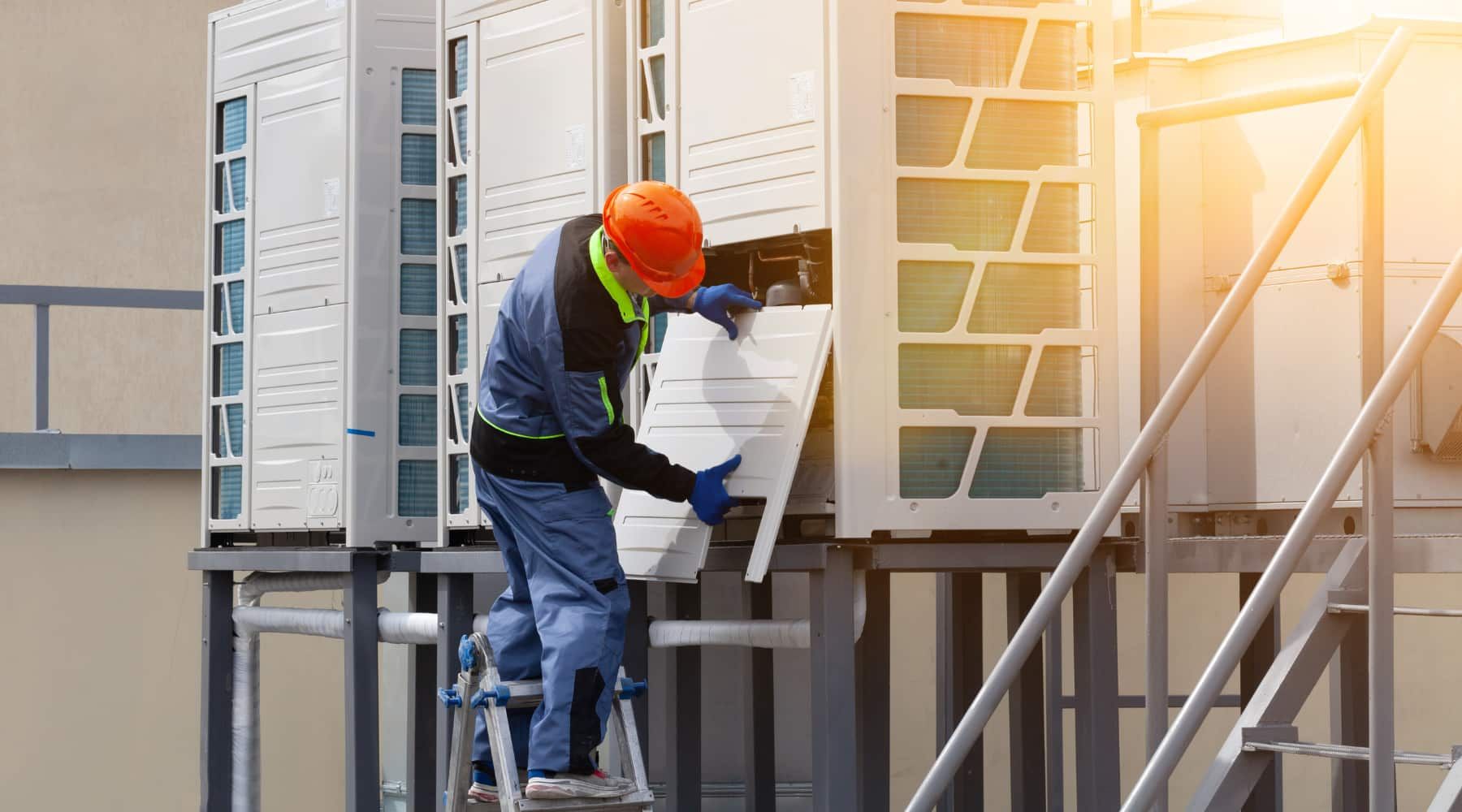Worker in orange hard hat installing siding on a house exterior in sunlight
