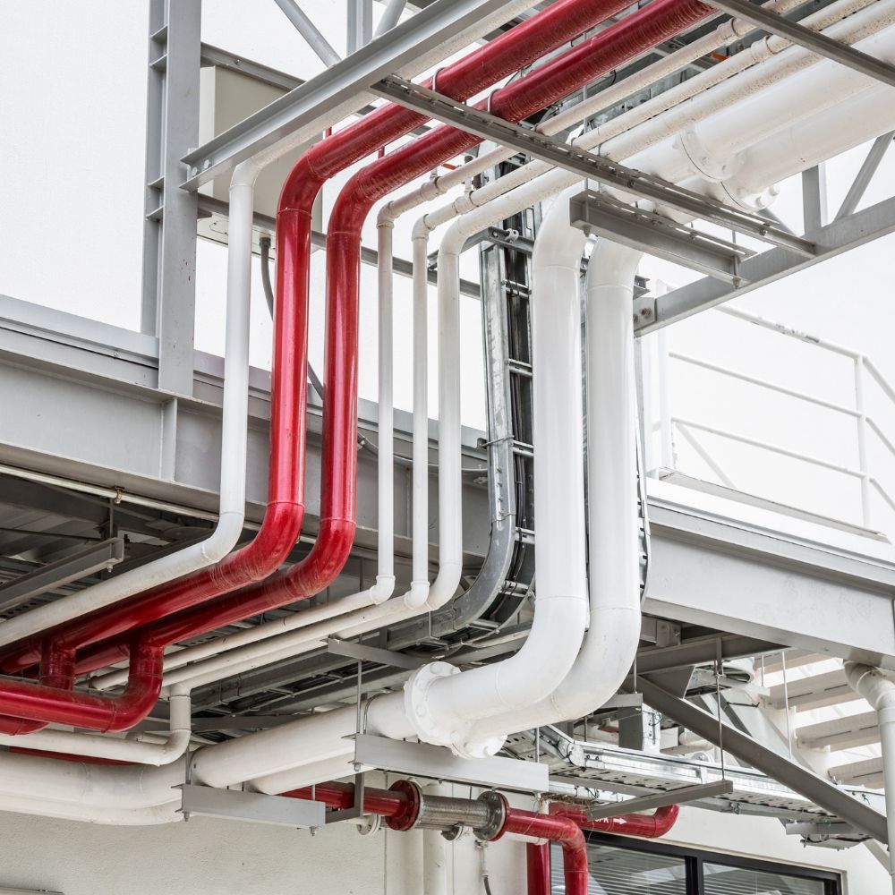 Industrial steel structure with red, gray, and white pipes running overhead on a bridge-like framework