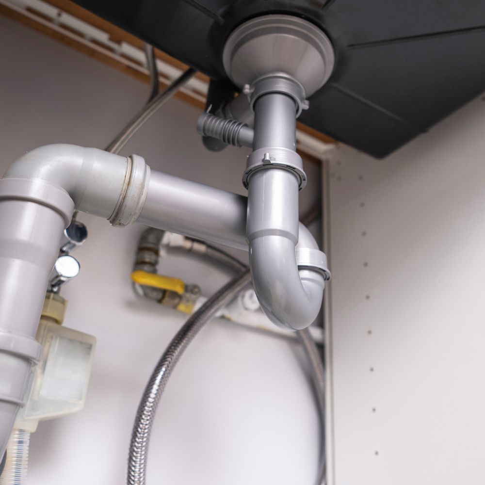 Close-up of a gray PVC P-trap and drainage assembly under a modern kitchen sink.
