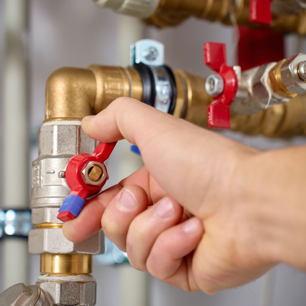 Close-up of a hand turning a red brass ball valve on a high-pressure plumbing line.