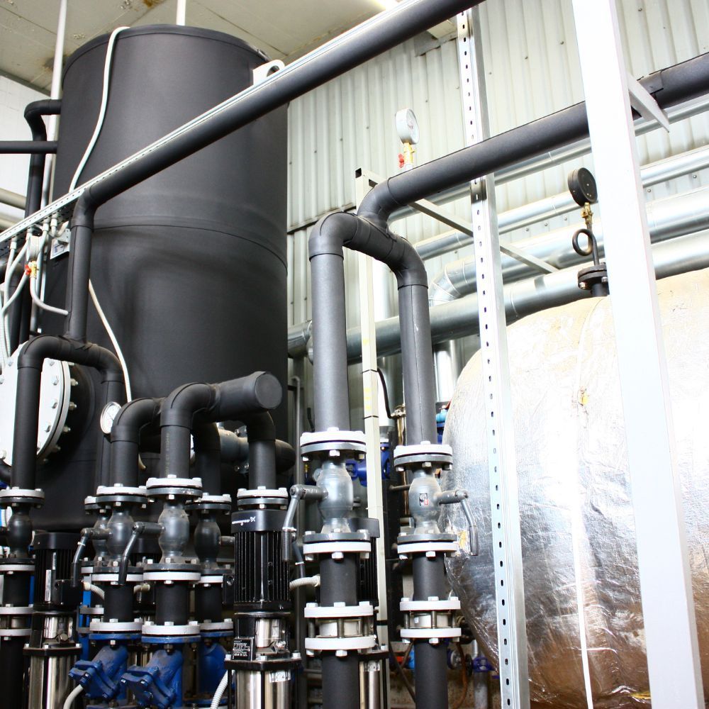 High-capacity insulated piping system connected to a large vertical storage tank and pressure gauges.