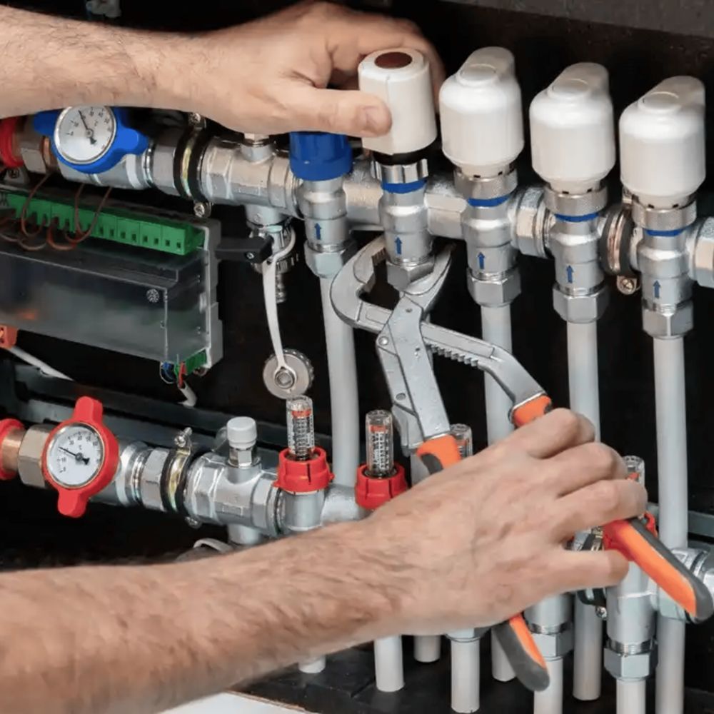 Technician using a plumbing wrench to adjust a radiant floor heating manifold and pressure valves.