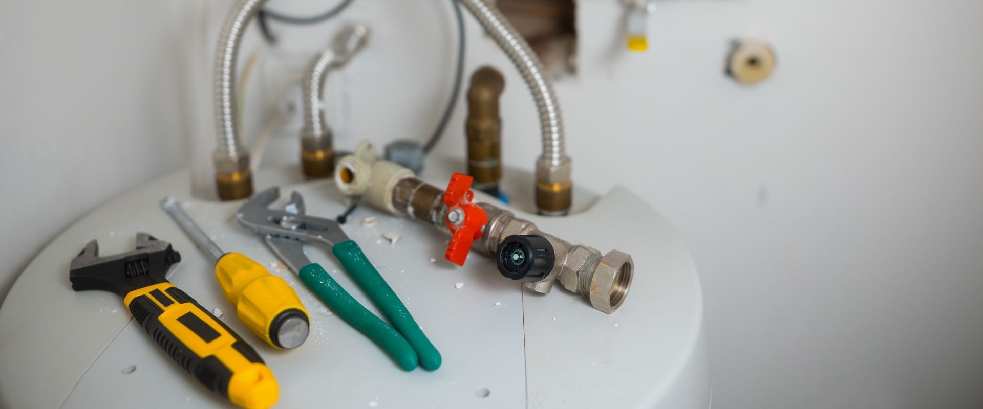 Plumbing tools, including a wrench, screwdriver, and pliers, resting on a white water heater with connected metal pipes.