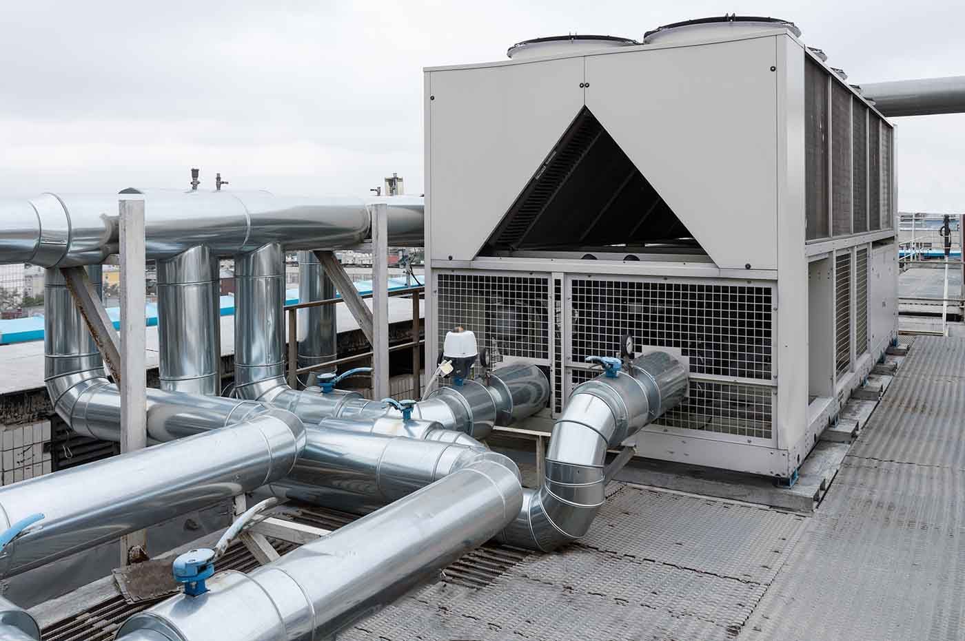 A large, industrial HVAC chiller unit with metallic piping installed on a rooftop.