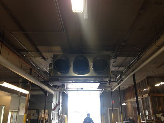 A large, three-nozzle air ventilation unit suspended from a commercial ceiling above an open warehouse loading bay.
