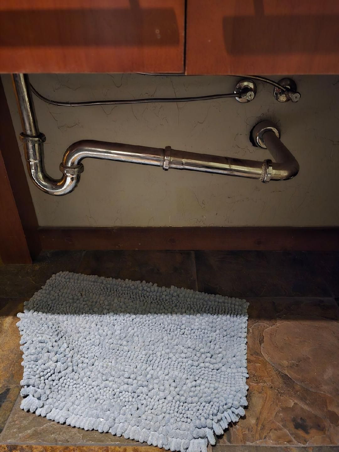 A bathroom sink with a plumbing pipe and a rug underneath it.